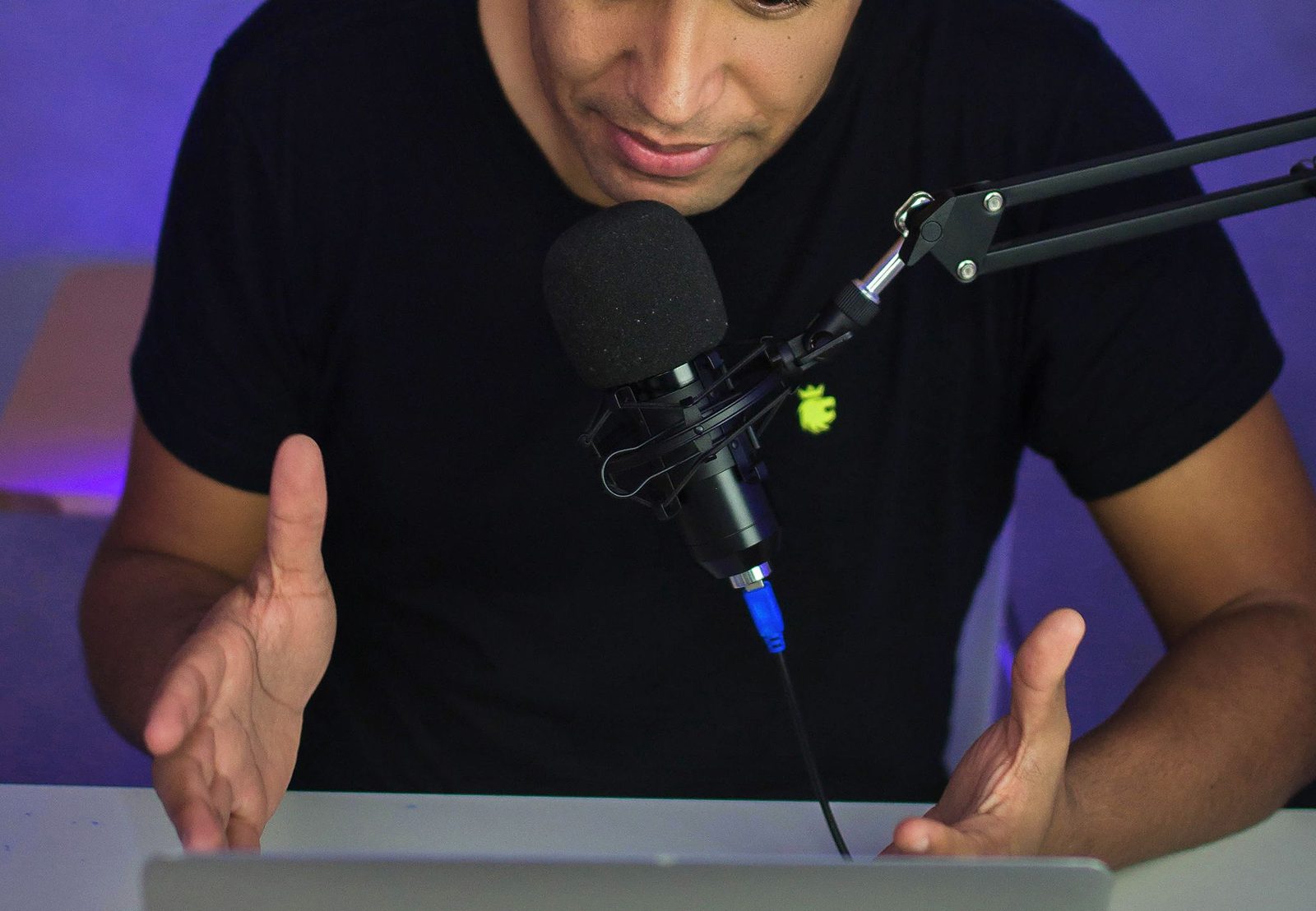 Podcaster speaking into a microphone while working from a laptop.