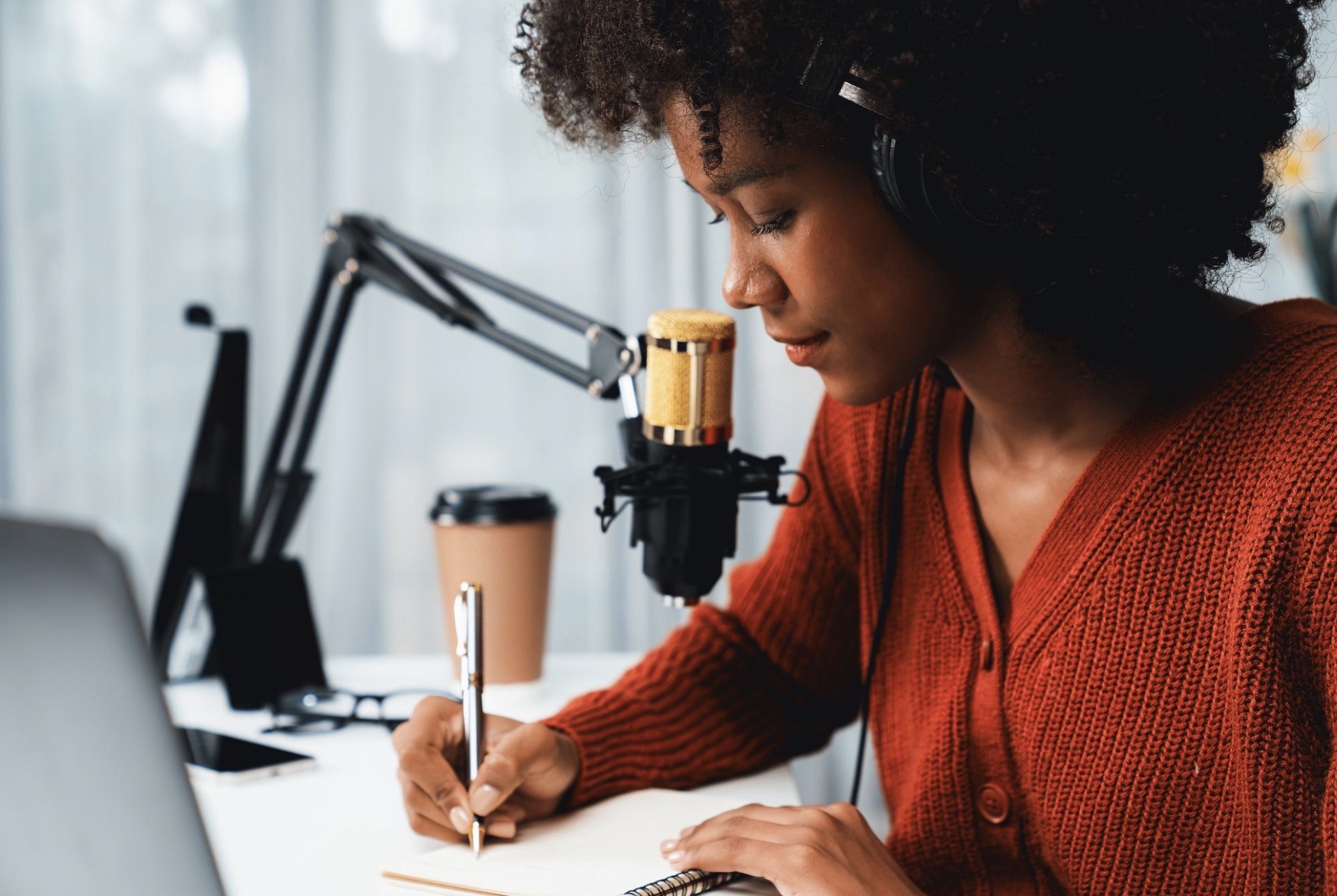 An author in red speaking into a gold desk microphone while drafting her book.